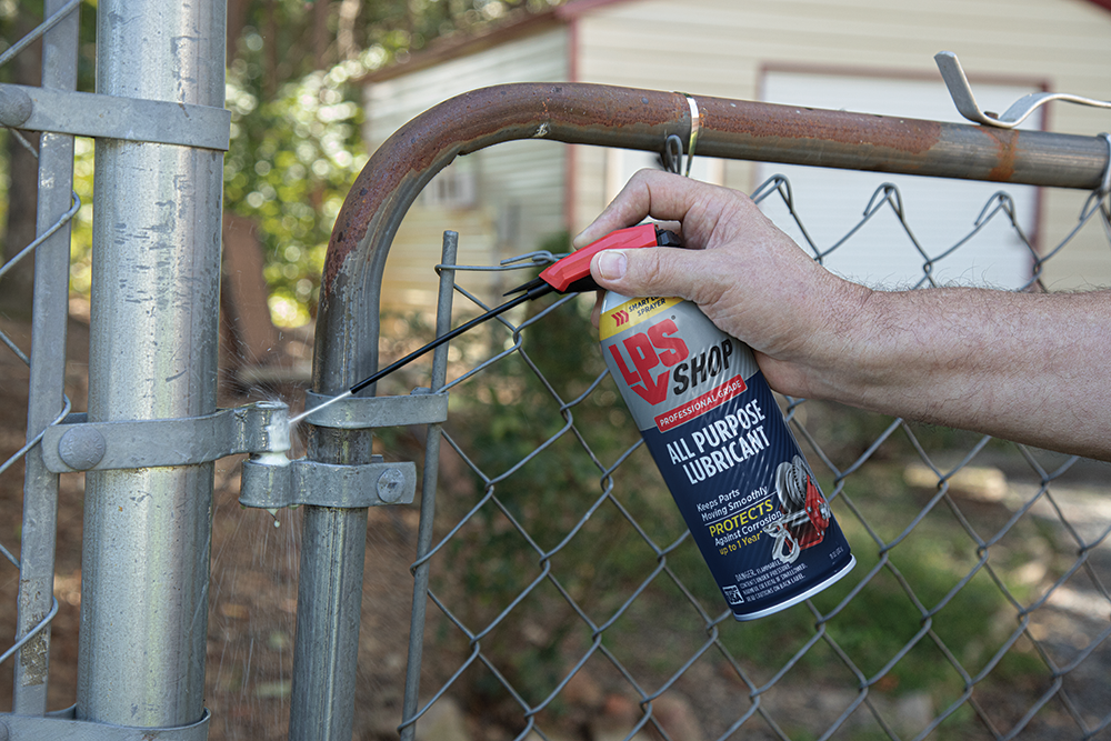 LPS Shop All Purpose Lubricant spraying fence door hinge.